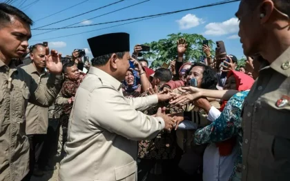 Presiden Prabowo Subianto berjabat tangan dengan warga yang antusias saat kunjungannya, dengan pengamanan ketat di sekitarnya.